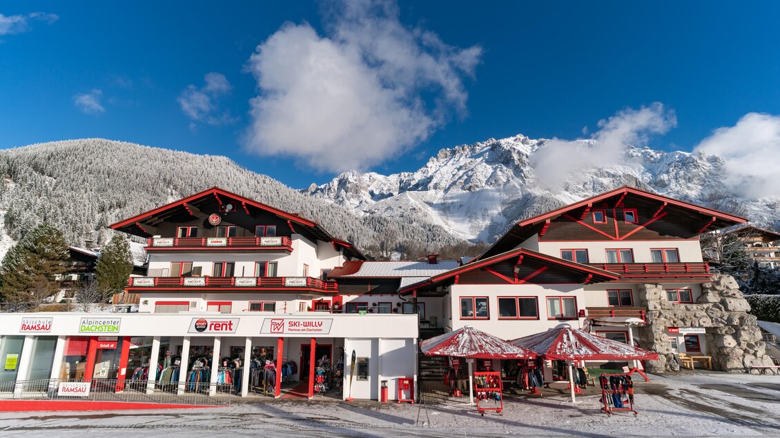 Ein malerisches Bergdorf mit schneebedeckten Bergen im Hintergrund. Im Vordergrund sind ein paar charmante Häuser mit roten Akzenten zu sehen. | © Ski Willy