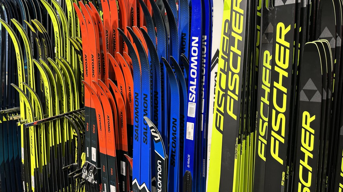 Eine Auswahl von Skiern in verschiedenen Farben, darunter Rot, Blau und Schwarz. Die Skier sind ordentlich aufgereiht und zeigen Markenlogos. | © SkiWilly