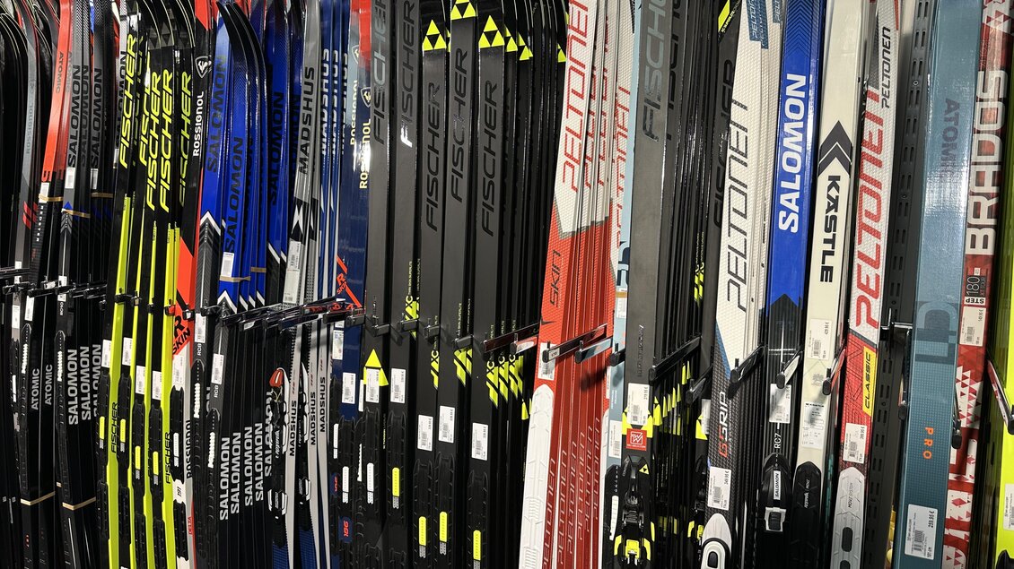 Eine große Auswahl an Langlaufskiern in verschiedenen Farben und Designs ist hier ausgestellt. Die Skier sind ordentlich an einem Regal angeordnet und zeigen die Markenvielfalt. | © SkiWilly