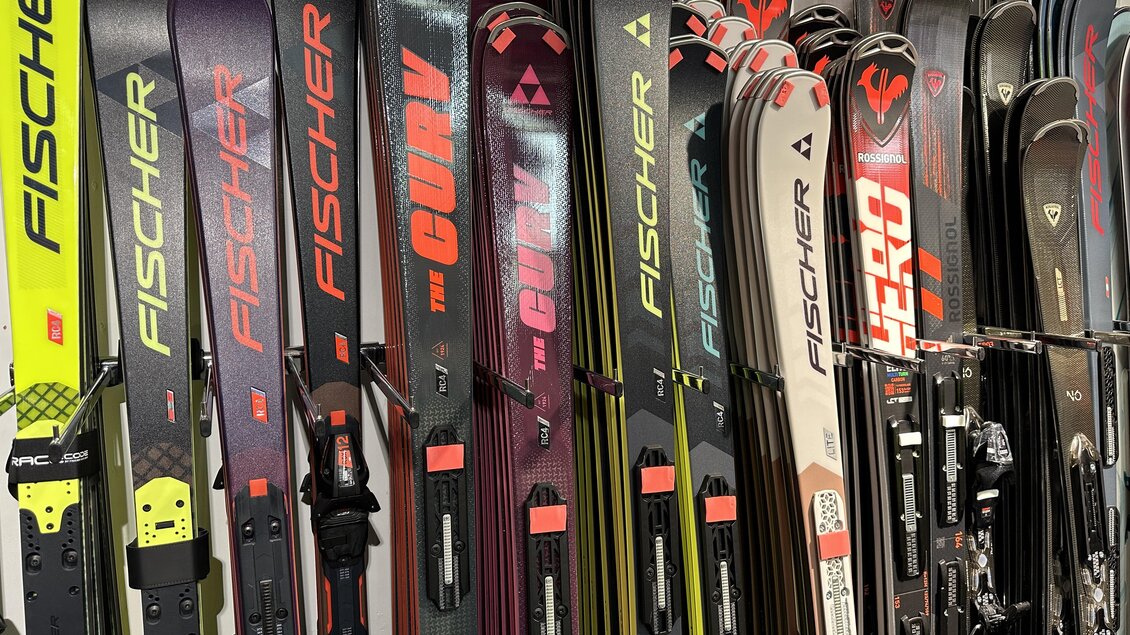 Eine Reihe von Skiern der Marke Fischer ist an einer Wand ausgestellt. Die Skier haben verschiedene Designs und Farben. | © SkiWilly
