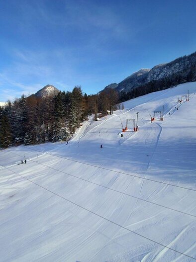 A snowy ski slope with several ski lifts in the background. The surroundings are surrounded by tall, green trees and mountains. | © Gottfried Wimmer