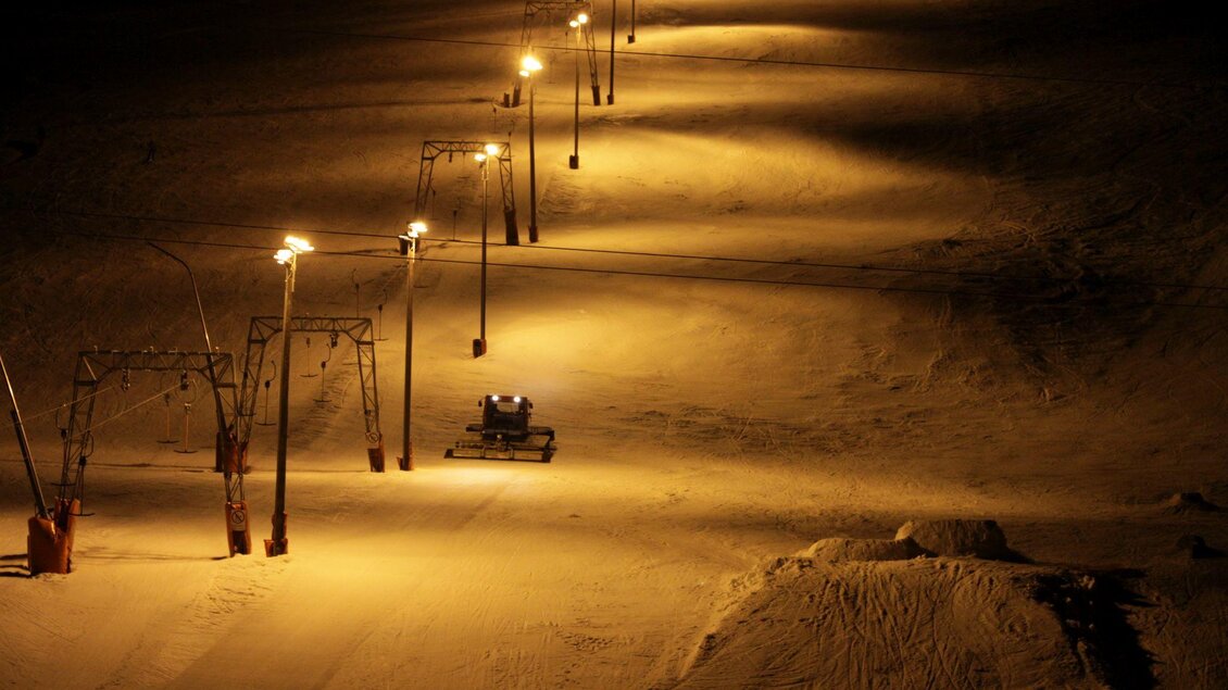 Eine beleuchtete Piste in der Nacht mit Schneekanonen und einem Pistenfahrzeug. Die Umgebung ist ruhig und die Schneefläche glänzt im Licht. | © Zlaim Lift