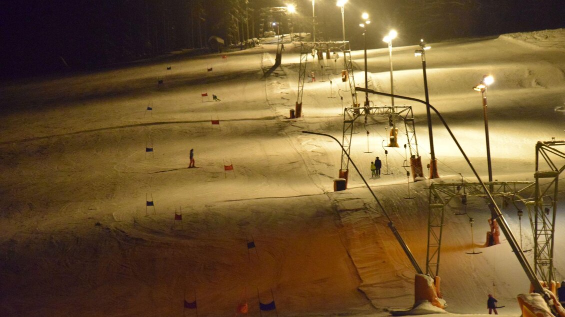Eine beleuchtete Skipiste bei Nacht mit Skifahrern und Schneekanonen. Die Szene zeigt eine ruhige Wintersportatmosphäre. | © Zlaim Lift