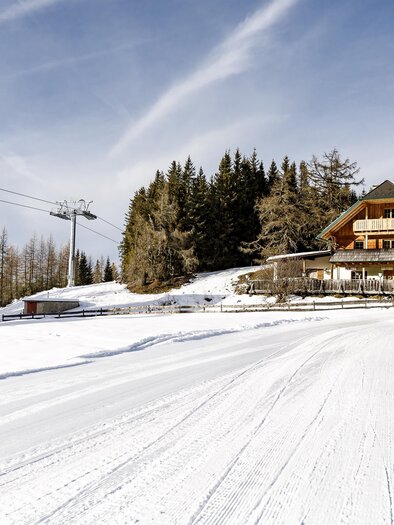 A picturesque mountain cabin in the snowy winter forest. Ski lifts soar over the calm landscape. | © Tourismusverband Murau