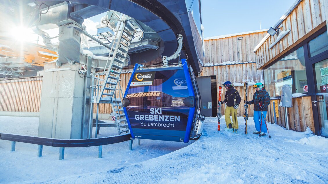 Eine moderne Seilbahnstation im Schnee mit Skifahrern, die auf den Aufstieg warten. Im Hintergrund sind Holzhütten und ein klarer Himmel zu sehen. | © Tourismusverband Murau