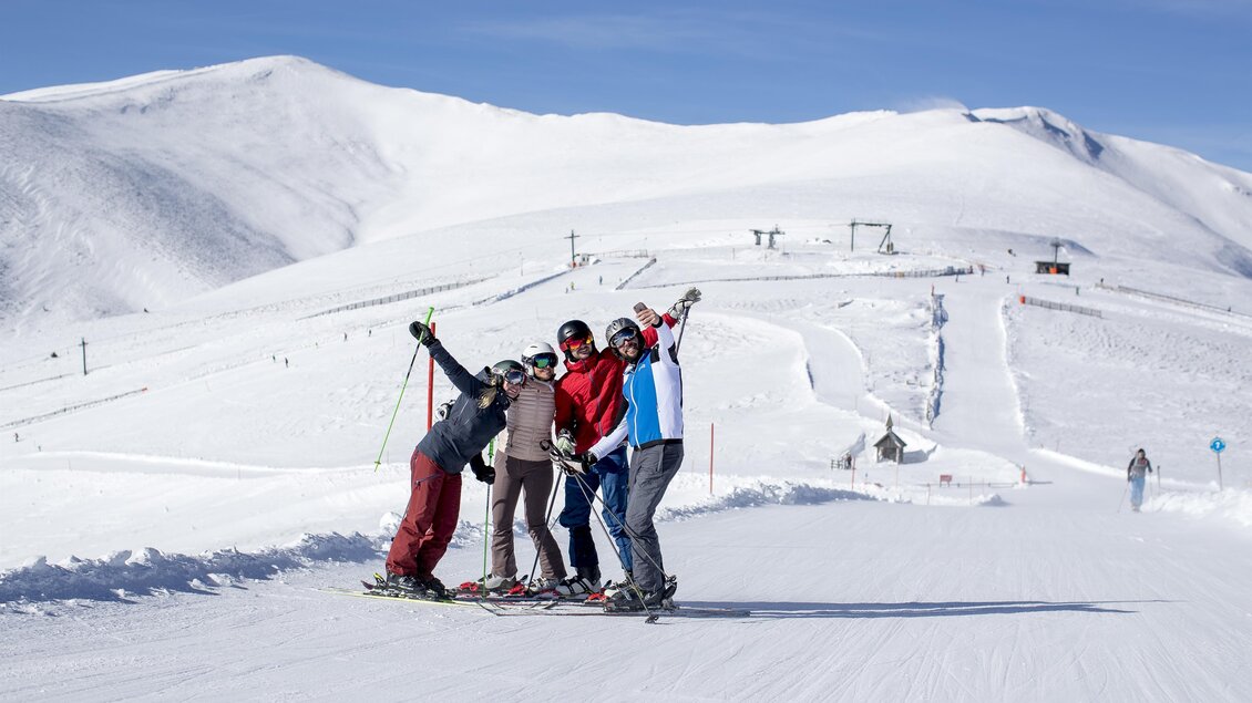 Eine Gruppe von Skifahrern posiert fröhlich auf der Piste. Im Hintergrund sind verschneite Berge und Skilifte zu sehen. | © Lachtal-Lifte u. Seilbahnen GmbH