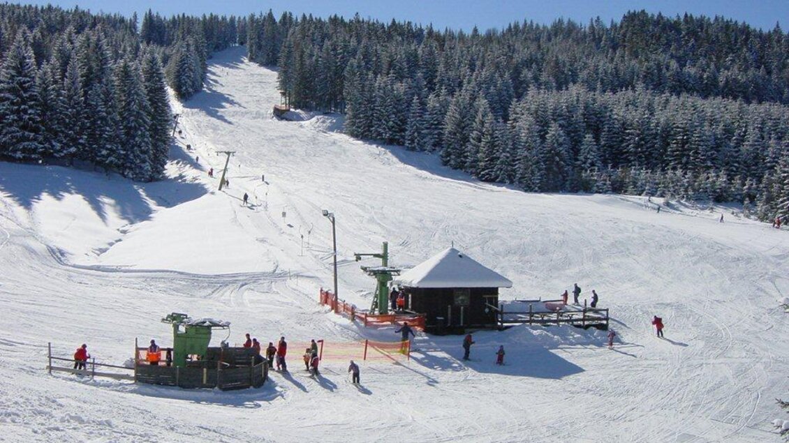Ein malerischer Skihang mit frisch gefallenem Schnee und Menschen, die Ski fahren. Im Hintergrund stehen dichte, schneebedeckte Bäume und eine Bergstation. | © Schigebiet Modriach-Winkel
