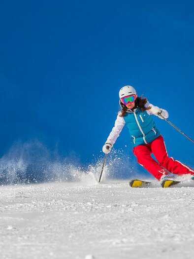 A skier is skiing down a snow-covered slope. The sky is clear and blue. | © coramax - Fotolia