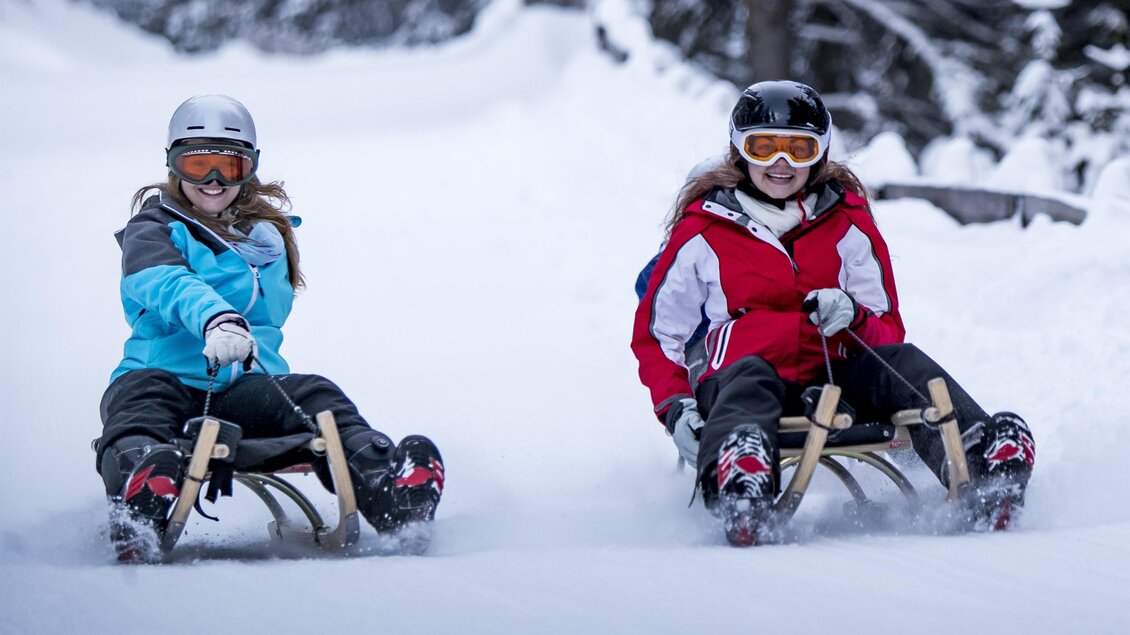 Zwei Personen fahren auf einem Rodel im Schnee. Sie tragen Helme und Wintersportkleidung. | © Tourismus Salzstiegl - Tom Lamm