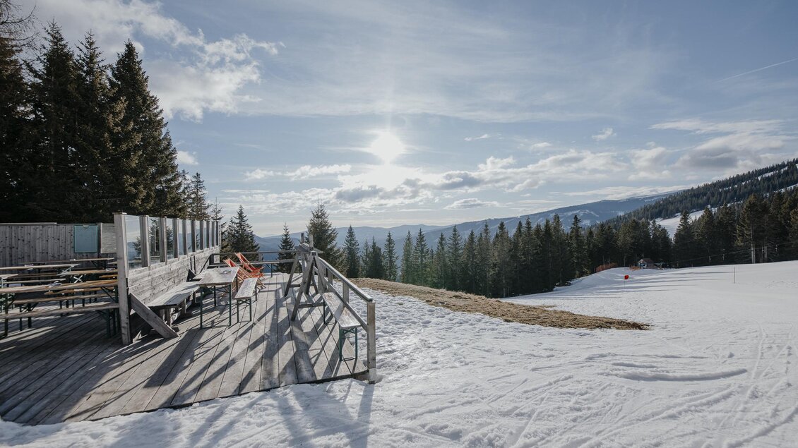 Eine verschneite Landschaft mit einem Holzsteg und einer Aussicht auf die umliegenden Berge. Im Hintergrund steht ein Wald, und der Himmel ist klar mit einigen Wolken. | © Salzstiegl - Nicole Seiser