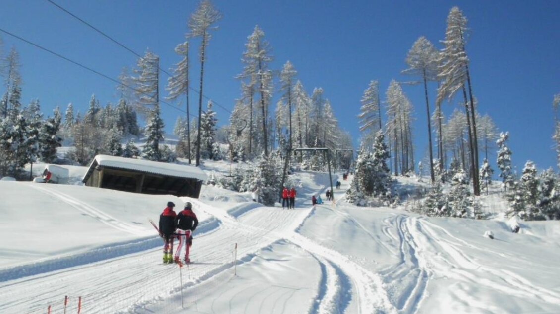 Eine verschneite Landschaft mit Skifahrern, die eine Piste hinaufgehen. Blauer Himmel und verschneite Bäume bilden eine idyllische Winterkulisse. | © Rudolf Sabetz