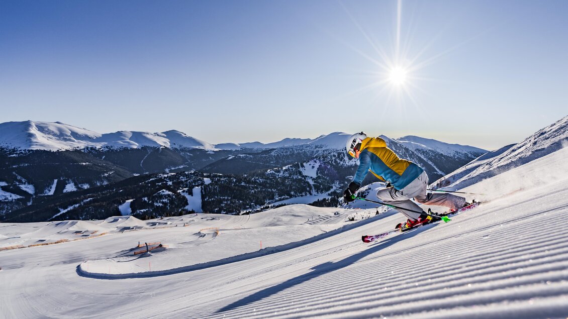 Ein Skifahrer fährt über eine verschneite Piste in den Bergen. Die Sonne scheint hoch am Himmel und der Ausblick ist atemberaubend. | © TMG Turracher Höhe Marketing GmbH