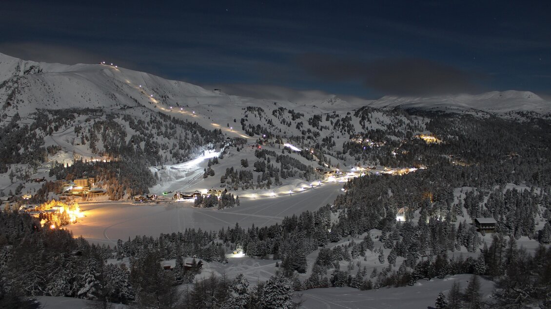 Eine winterliche Landschaft mit einem schneebedeckten See und beleuchteten Hügeln. Der Nachthimmel ist klar und die Umgebung strahlt eine ruhige Atmosphäre aus. | © TMG Turracher Höhe Marketing GmbH