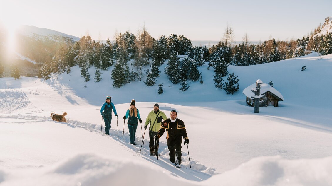 Eine Gruppe von Menschen wandert durch eine schneebedeckte Landschaft. Im Hintergrund sind Bäume und eine kleine Hütte zu sehen. | © TMG Turracher Höhe Marketing GmbH