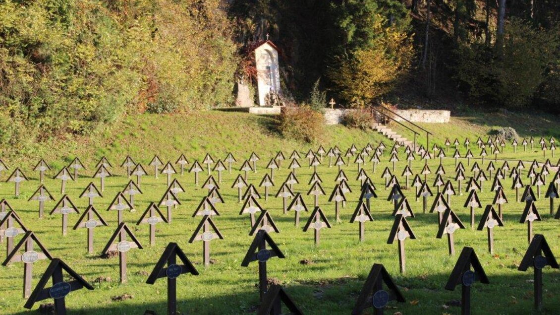 Ein ruhiger Friedhof mit vielen kleinen Holzkreuzen, umgeben von Bäumen. Im Hintergrund ist eine Kapelle sichtbar. | © Marktgemeinde St. Michael