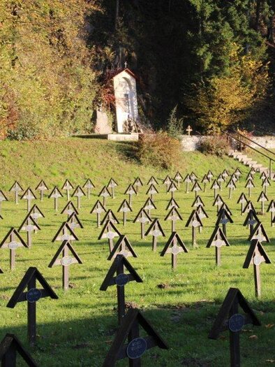 A peaceful cemetery with many small wooden crosses, surrounded by trees. In the background, a chapel is visible. | © Marktgemeinde St. Michael