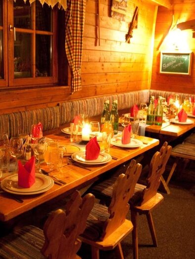 A cozy restaurant with wooden furniture and festively set tables. Red napkins and candlelight create an inviting atmosphere. | © Sonnenalm