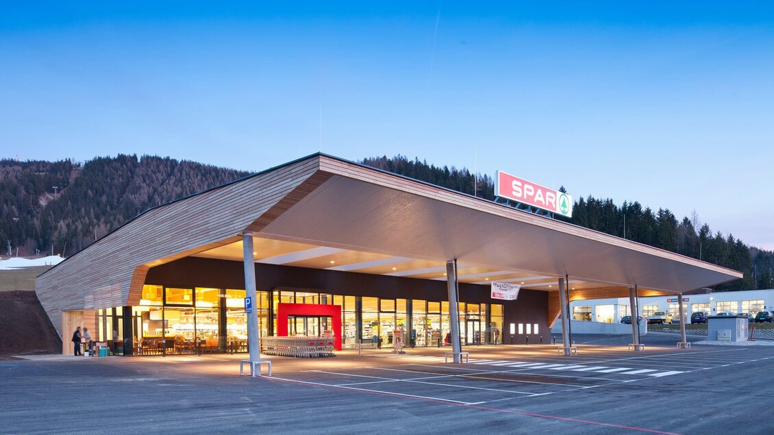 Ein moderner Supermarkt mit einem großen Vordach und vielen Fenstern. Im Hintergrund sind Wälder und Berge sichtbar. | © www.sparsteiner.at