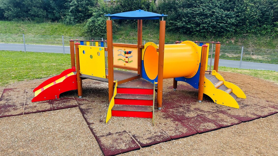 Ein farbenfrohesSpielplatzgerät mit einer Rutsche, einem Tunnel und einem kleinen Dach. Der Bereich ist mit Gummigranulat ausgelegt und von Rasen umgeben. | © Tourismus Vorau