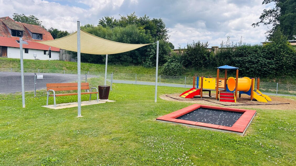 Ein Spielplatz mit einer bunten Rutsche und einer Wippe steht in einer grünen Wiese. Neben dem Spielbereich gibt es eine Bank und ein Trampolin. | © Tourismus Vorau