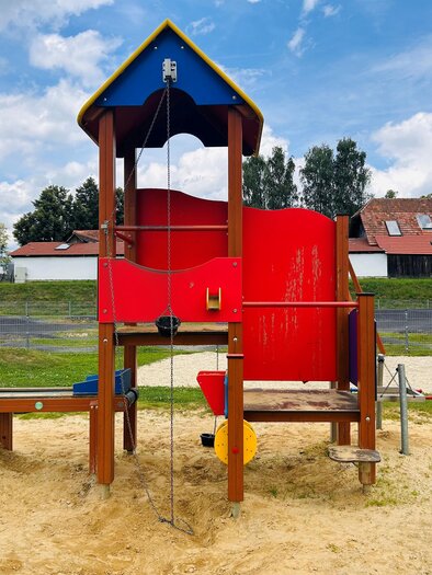 A playground with a colorful slide and a wooden climbing structure. The area is surrounded by sand and there are some trees in the background. | © Tourismus Vorau
