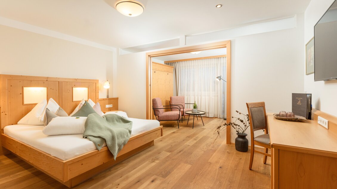 Ein modernes Schlafzimmer mit einem großen Bett und gemütlicher Holzdekoration. Der Raum verfügt über einen Sitzbereich und viel natürliches Licht. | © Bärenwirt