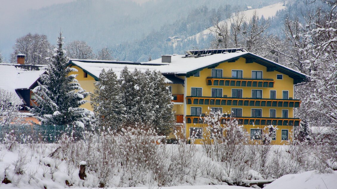Ein gelbes Hotel steht in einer verschneiten Landschaft. Umgeben von Bäumen und Bergen zeigt es die winterliche Schönheit der Natur. | © Bärenwirt