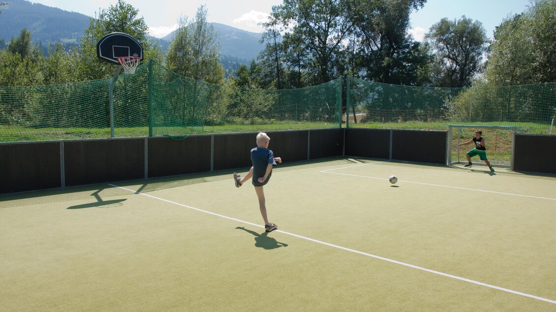 Ein Kind schießt einen Fußball auf ein Tor, während ein anderer Junge im Tor steht. Im Hintergrund sind Bäume und Berge zu sehen. | © Bärenwirt