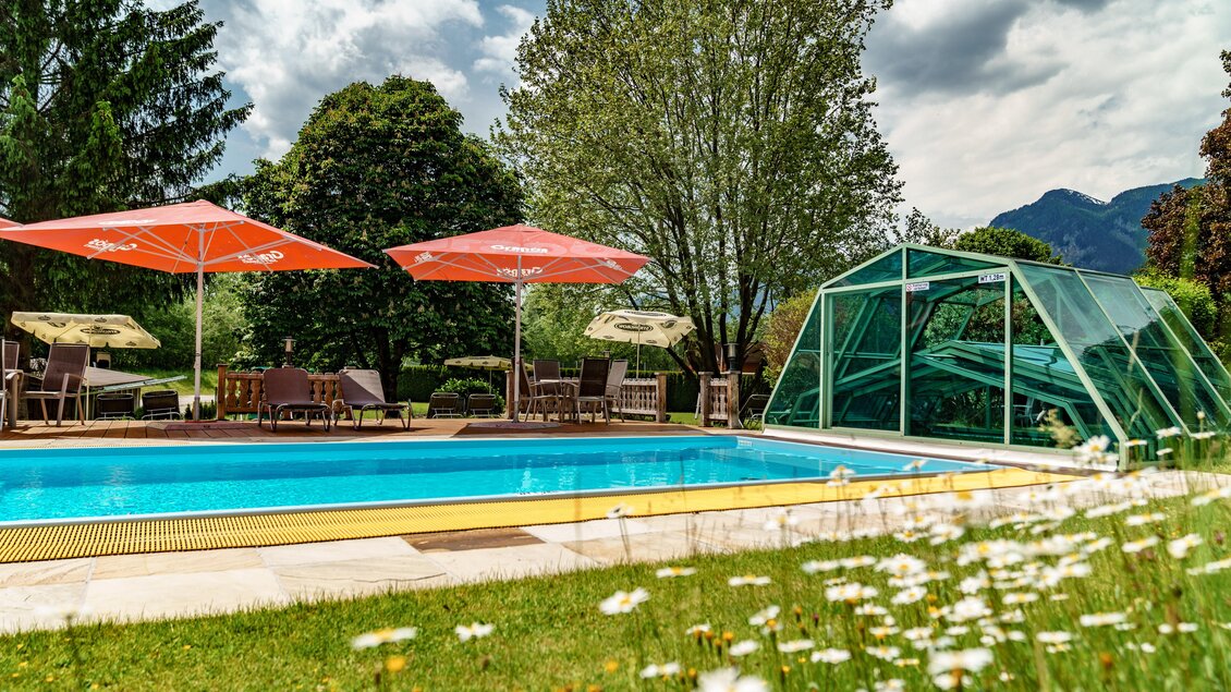 Ein schöner Swimmingpool umgeben von grünen Wiesen und sonnigen Schirmen. Im Hintergrund sind Bäume und Berge zu sehen. | © Bärenwirt