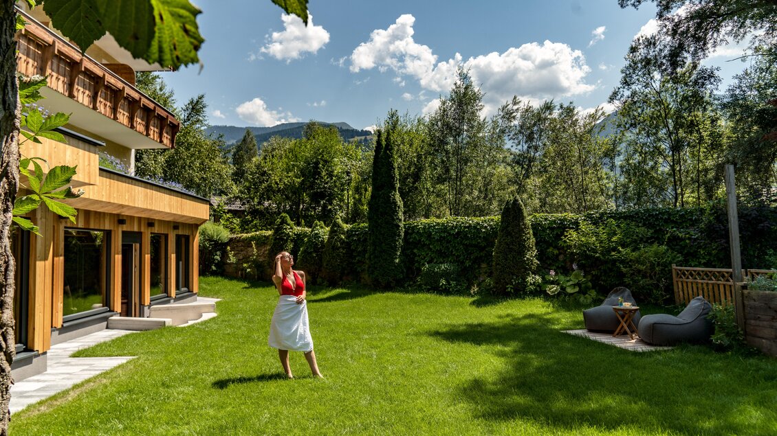 Ein schöner Garten mit grünem Rasen und Bäumen. Im Hintergrund steht ein modernes Haus unter einem klaren blauen Himmel. | © baerenwirt.com