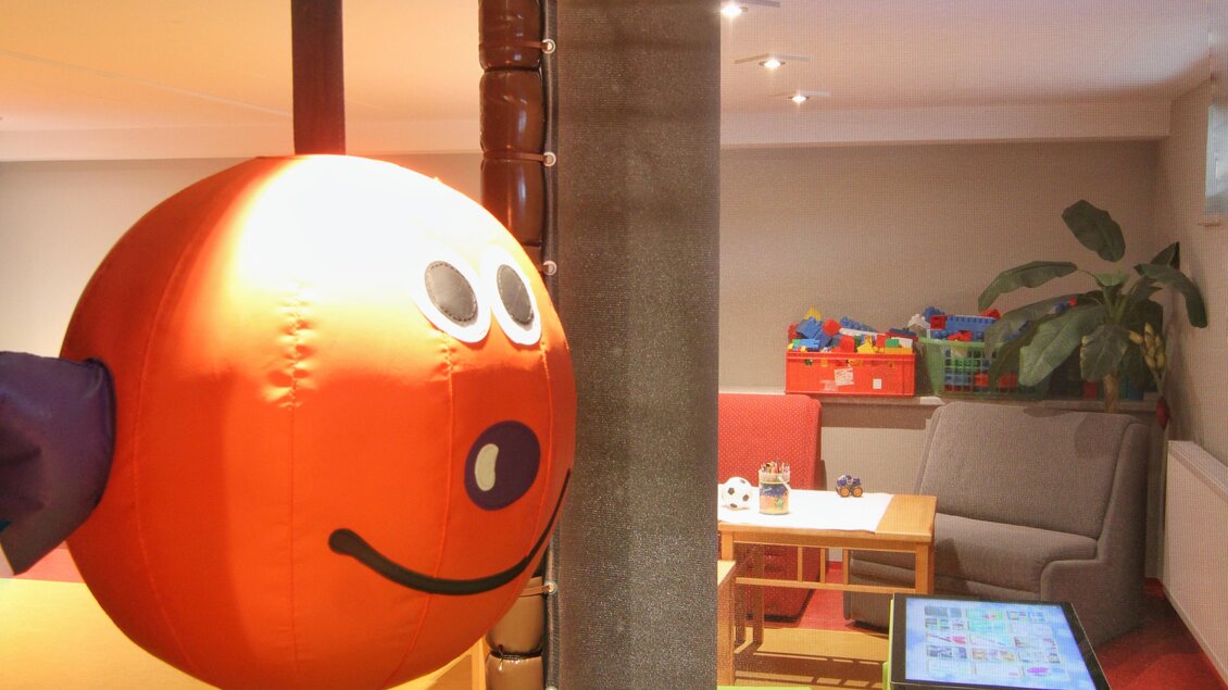 Ein Spielbereich mit einem großen orangefarbenen Ball und einem Netz. Im Hintergrund sind gemütliche Sitzgelegenheiten und Spielzeug zu sehen. | © baerenwirt.com