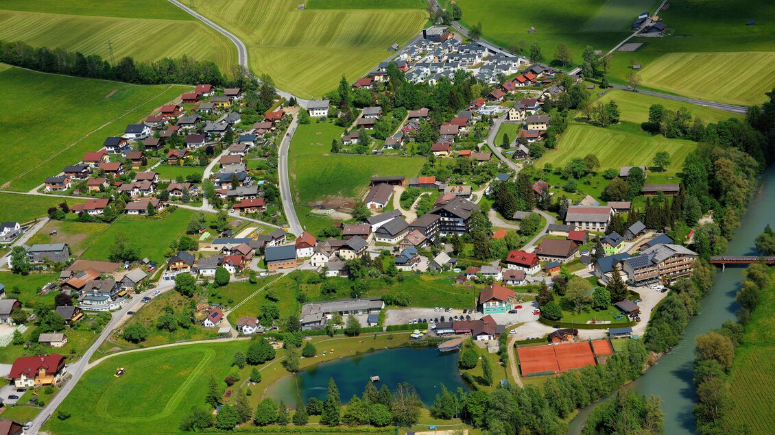 Eine malerische Landschaft mit einem kleinen Dorf, umgeben von grünen Feldern und einem ruhigen Teich. Die Häuser sind bunt und harmonisch in die Natur eingebettet. | © baerenwirt.com