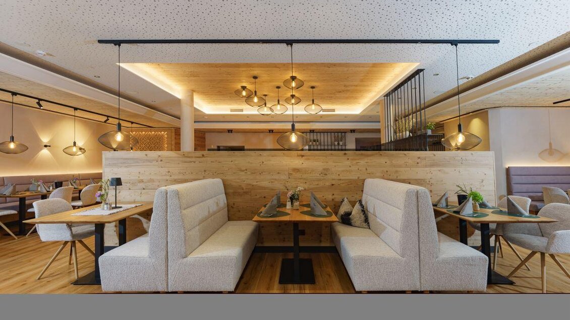Heller Restaurantbereich mit modernen Sitznischen aus hellem Stoff, Holzwänden und eleganter Beleuchtung. Die Tische sind liebevoll mit Servietten und Blumen dekoriert, die Atmosphäre wirkt gemütlich und einladend. | © Bärenwirt