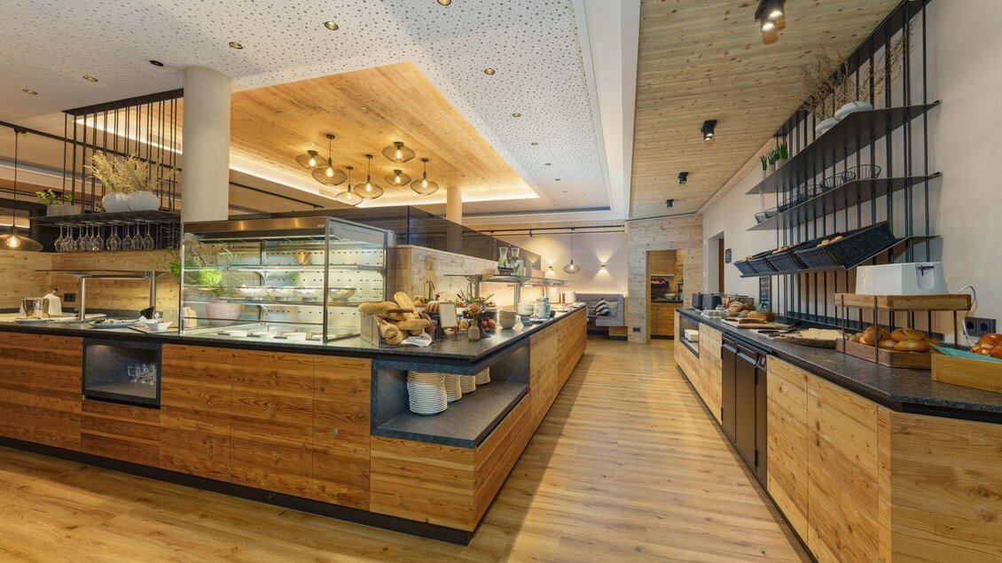 Moderner Buffetbereich mit warmem Holzdesign, schwarzen Arbeitsplatten und stilvoller Beleuchtung. Auf den Theken stehen Brote, Schalen und Speisen bereit, im Hintergrund ist ein gemütlicher Sitzbereich zu sehen. | © Bärenwirt