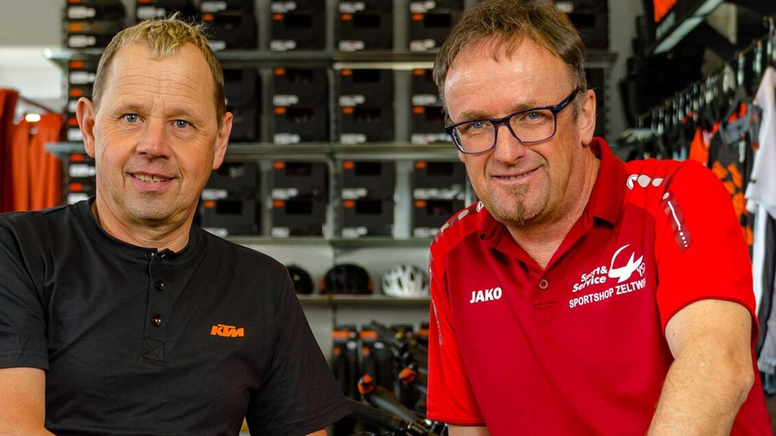 Zwei Männer stehen lächelnd in einem Fahrradgeschäft. Im Hintergrund sind Fahrräder und Bekleidung sichtbar. | © Josef Rabensteiner