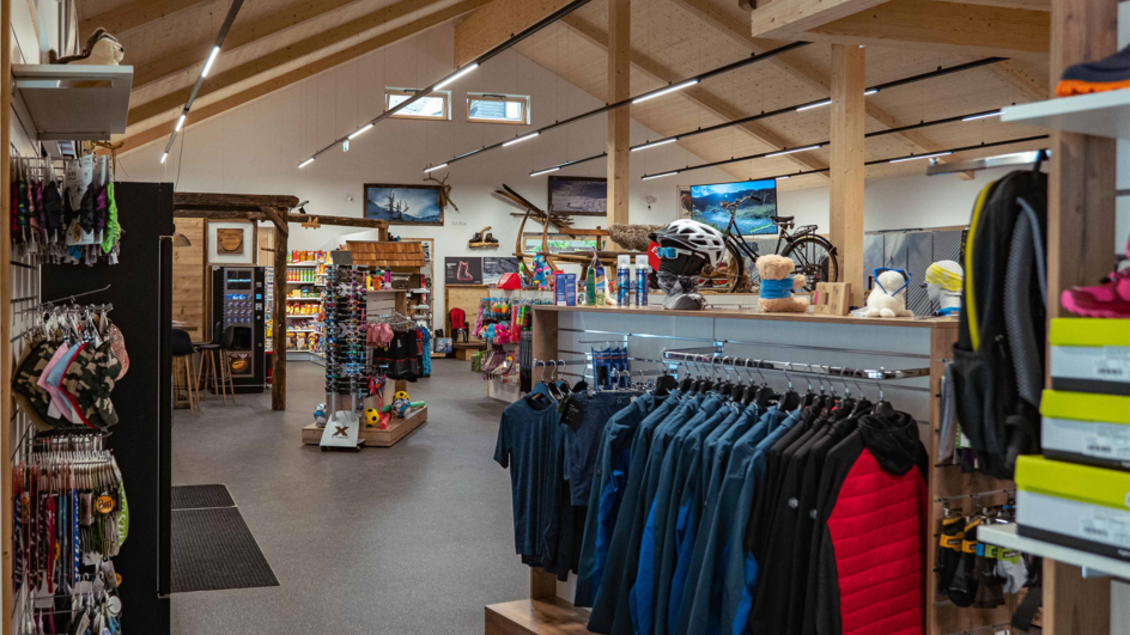 Ein moderner Sportladen mit Holzdecke und viel Licht. Im Vordergrund sind Kleidung und Ausrüstung für Outdoor-Aktivitäten zu sehen. | © Sport Scherz