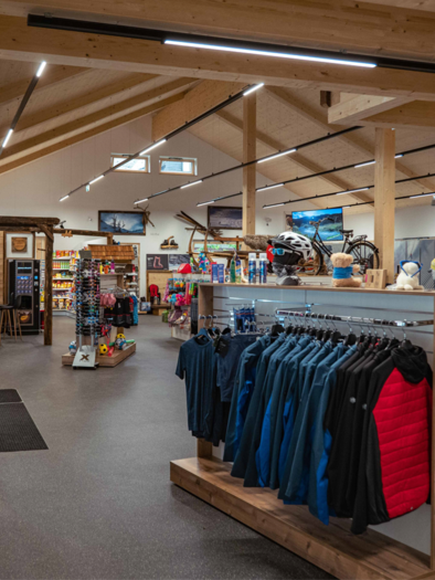 A modern sports store with a wooden ceiling and plenty of light. In the foreground, clothing and equipment for outdoor activities can be seen. | © Sport Scherz