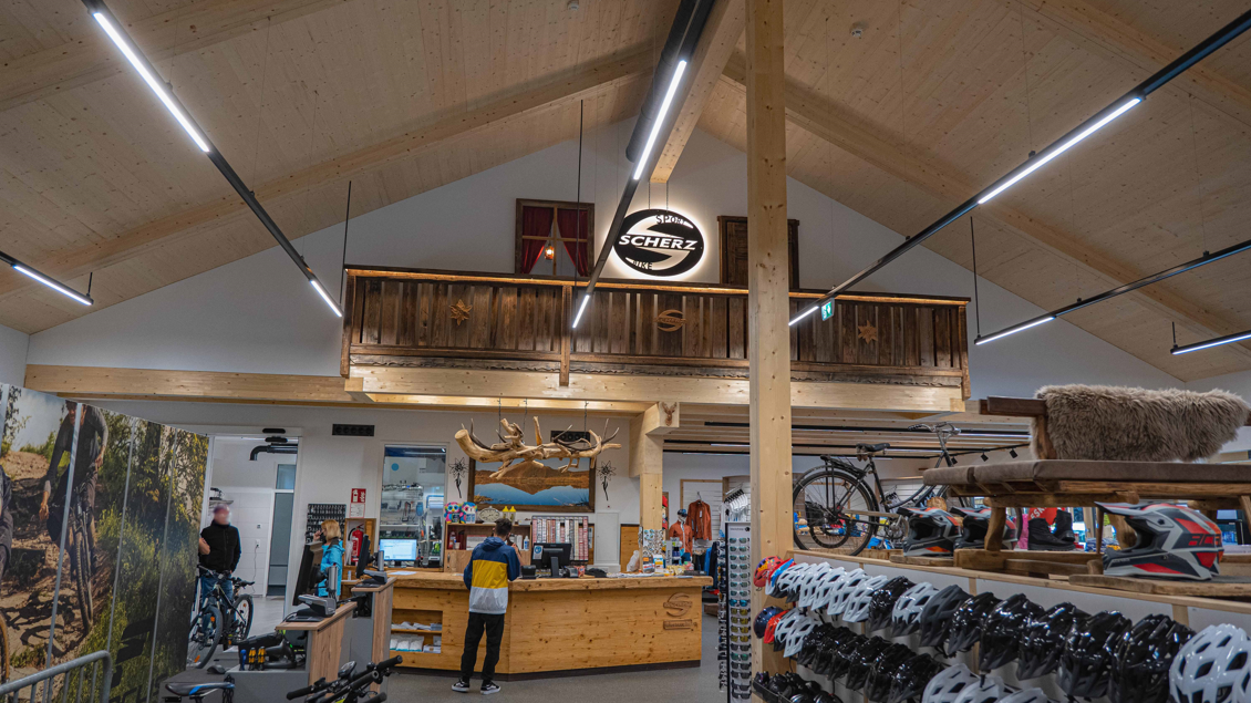 Ein Innenraum eines Geschäfters mit hohen Decken und Holzdetails. Der Bereich ist gut beleuchtet und zeigt Fahrräder sowie Helme zum Verkauf. | © Sport Scherz