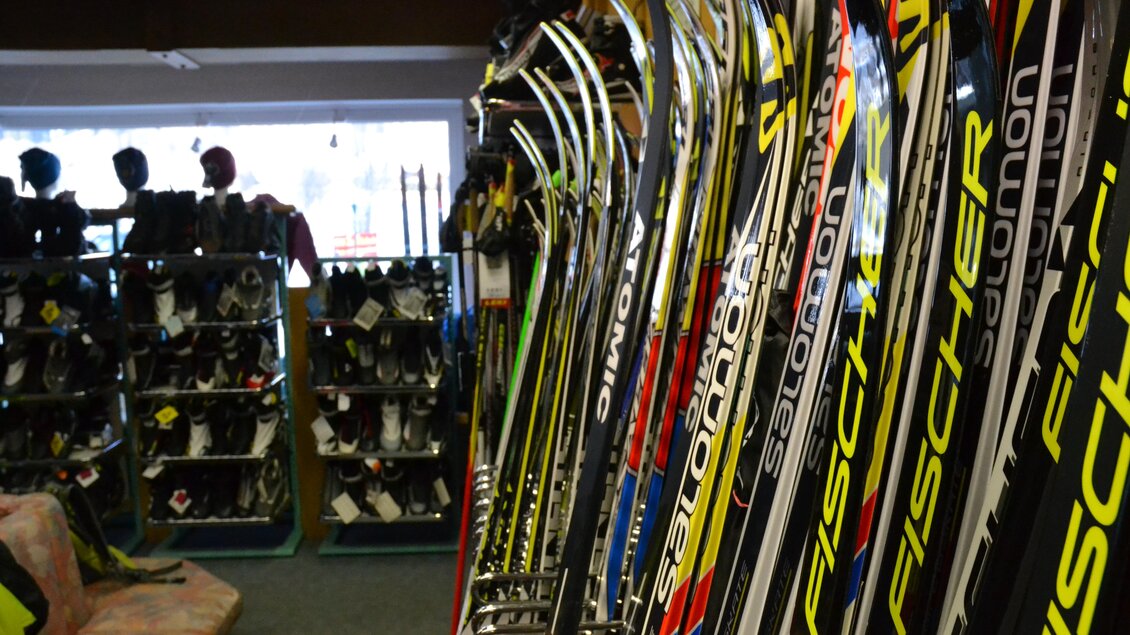 Ein Sportgeschäft mit einer Auswahl an Skiern und Skischuhen. Im Hintergrund sind einige Kunden und eine farbenfrohe Anzeige zu sehen. | © Sport Steiner 