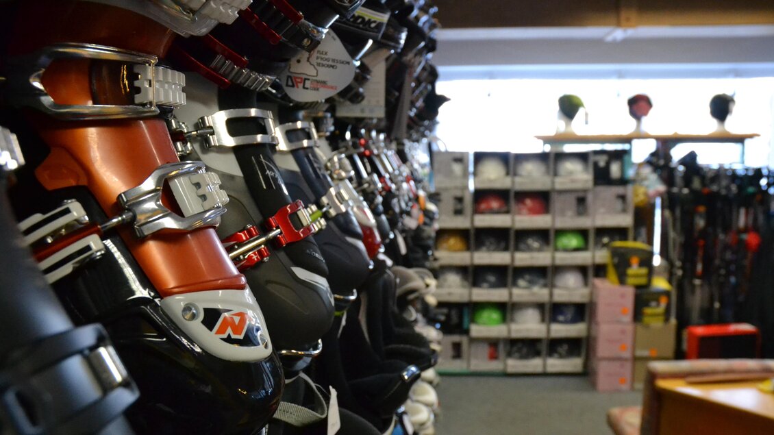 Ein Sportgeschäft mit einer Reihe von Skibindungen in der Vordergrundperspektive. Im Hintergrund sind verschiedene Sporthelme und Ausrüstungen auf Regalen sichtbar. | © Sport Steiner 