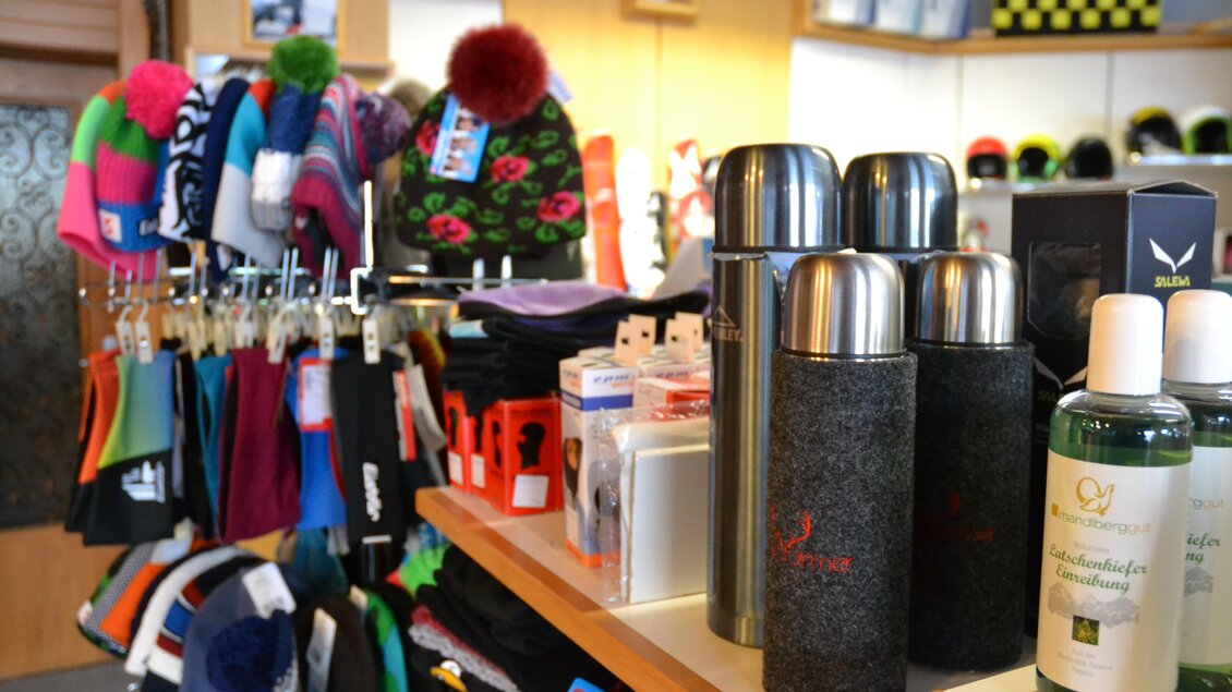 Ein Geschäft mit Winteraccessoires wie Mützen und Schals. Im Vordergrund stehen Thermosflaschen und Pflegeprodukte auf dem Tisch. | © Sport Steiner 