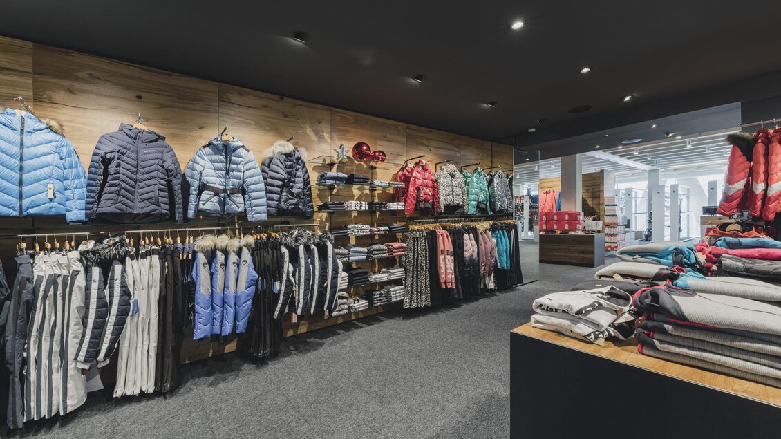 Ein moderner Bekleidungsladen mit einer Auswahl an Winterjacken und Sweatshirts. Die Kleidung ist ordentlich an Regalen und Kleiderständern präsentiert. | © Sport Tritscher Shop in Rohrmoos