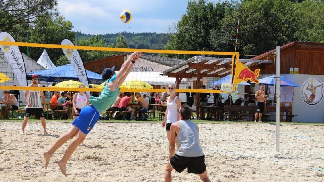 Ein Sandvolleyballspiel im Freien mit mehreren Spielern. Im Hintergrund sind Sonnenschirme und Sitzbereiche zu sehen. | © FZC Bad Waltersdorf