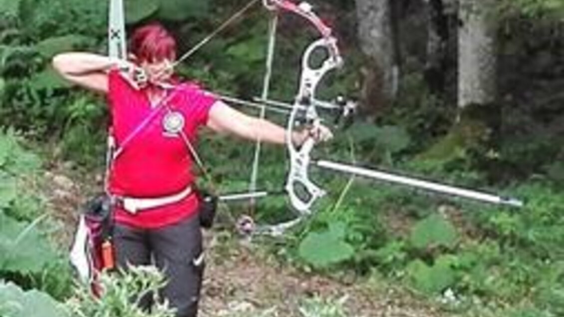 Eine Person mit rotem T-Shirt zielt mit einem modernen Bogen in einem Wald. Um sie herum sind viel Grün und Bäume zu sehen. | © Jeitler Heidi