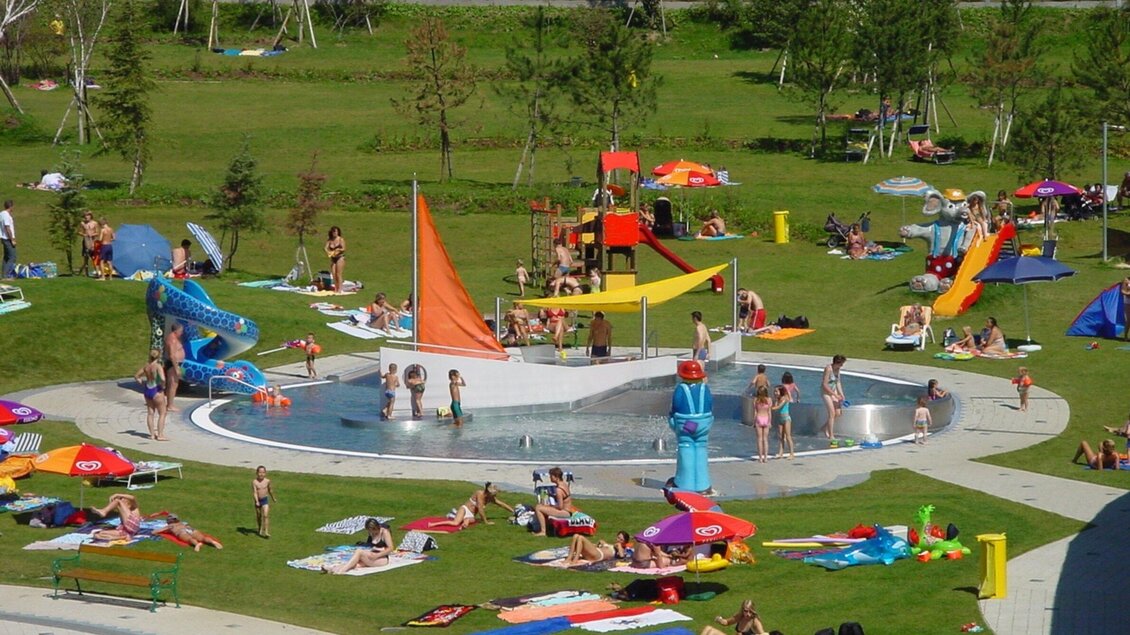 Die belebte Freizeitanlage Frohnleiten mit Kinderplantschbecken und Rutschen. Viele Kinder und Familien entspannen auf der Wiese und genießen die Sonne. | © TV Region Graz - Rene Vidalli