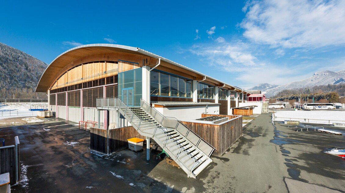 Ein modernes Gebäude mit einer geschwungenen Dachform und großen Fenstern. Es befindet sich in einer bergigen Umgebung mit klarem Himmel. | © TV Region Graz - Rene Vidalli