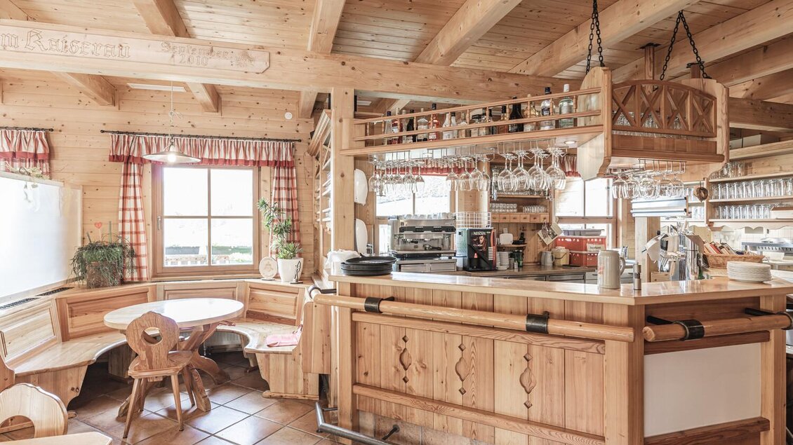Eine gemütliche Holzbar mit hölzernen Möbeln und einem warmen, einladenden Ambiente. Fenster mit Vorhängen lassen Tageslicht herein und schaffen eine freundliche Atmosphäre. | © Thomas Sattler