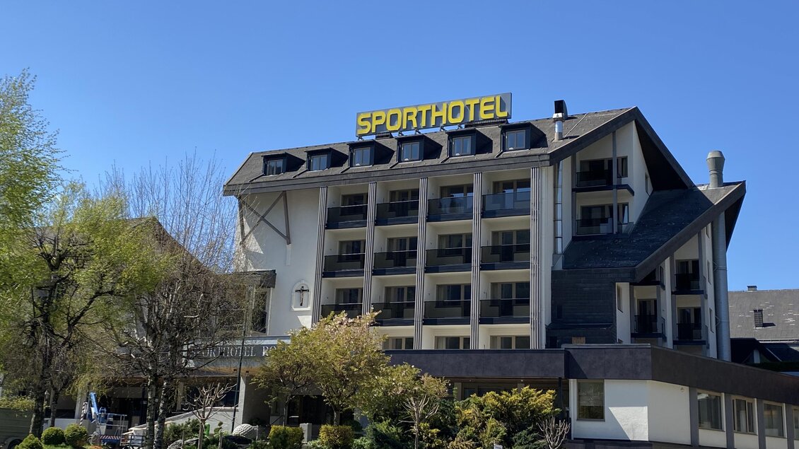 Ein modernes Sporthotel mit einer einladenden Fassade. Umgeben von grüner Landschaft und klarem blauem Himmel. | © Maria Kindler