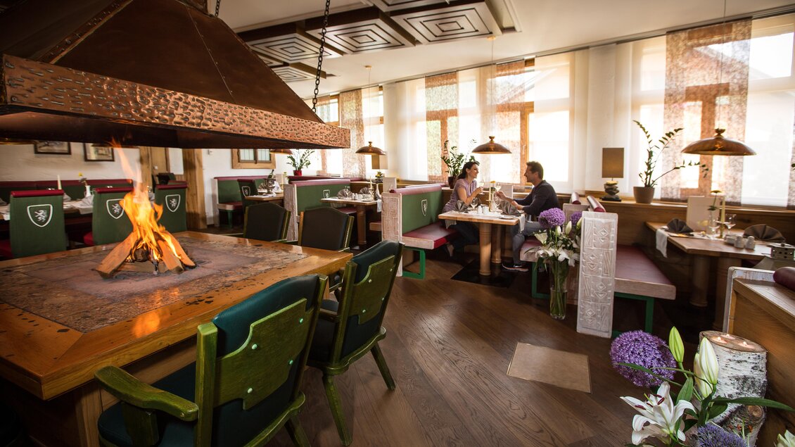 Ein gemütliches Restaurant mit einem offenen Kamin und elegantem Interieur. Gäste sitzen an Tischen, während die Sonne durch große Fenster scheint. | © Schatzl Fotos