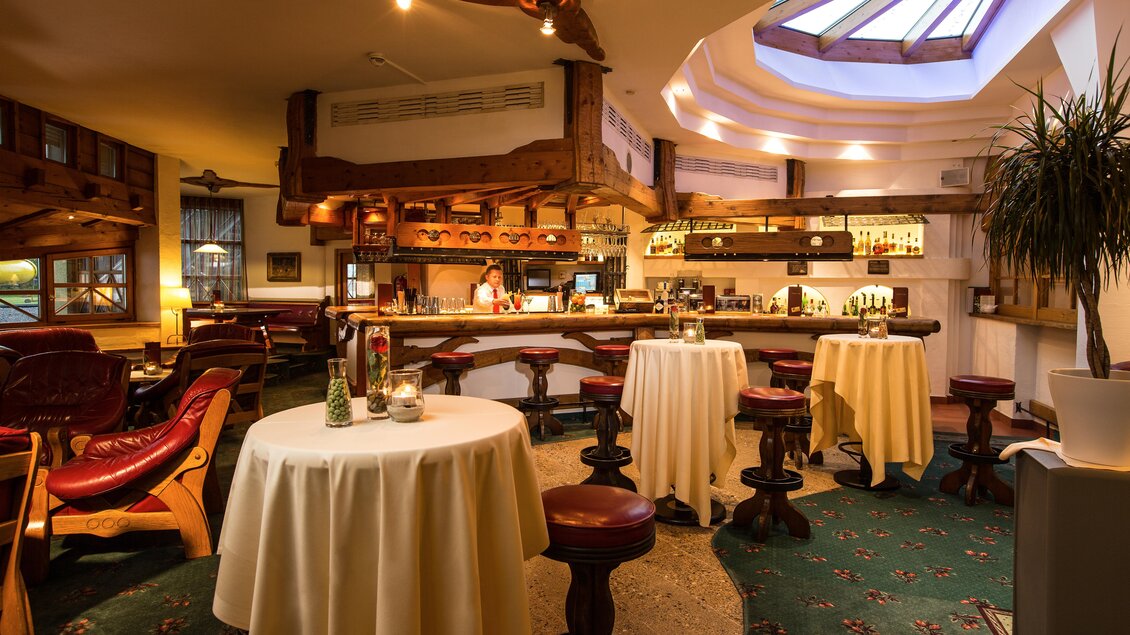 Ein stilvolles Restaurant mit einer bar und runden Tischen. Die gemütliche Atmosphäre wird durch Holzverzierungen und eine helle Decke mit Oberlichtern unterstrichen. | © Sporthotel Royer